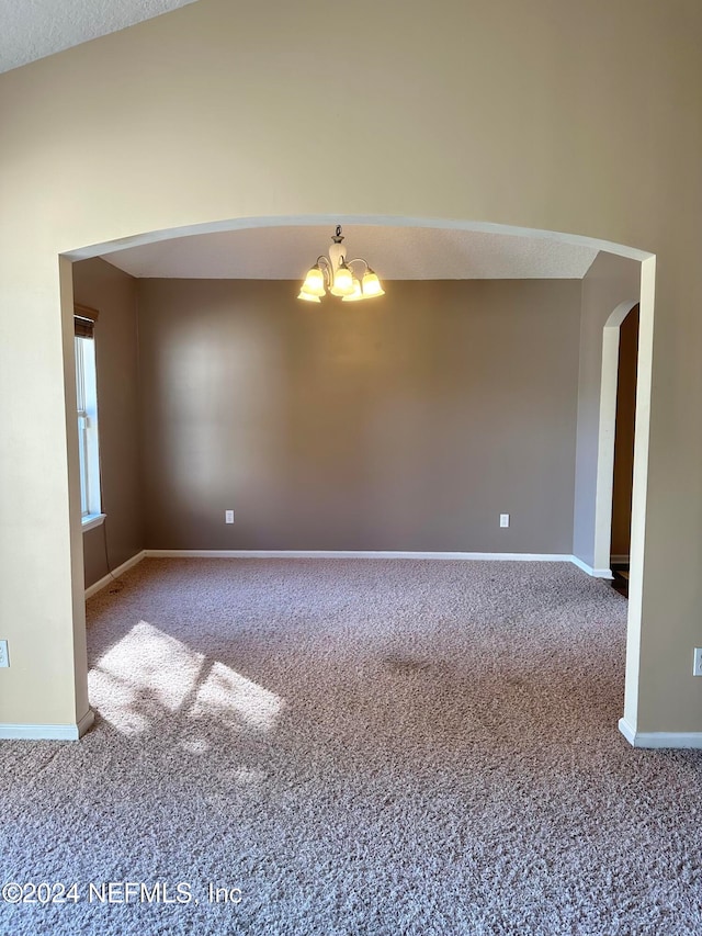 empty room featuring a textured ceiling, vaulted ceiling, a notable chandelier, and carpet floors