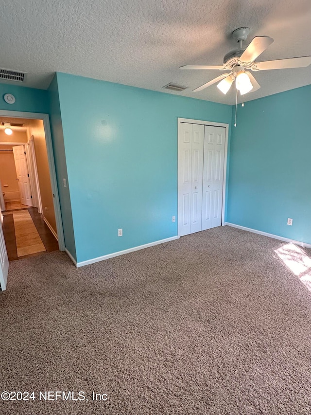 unfurnished bedroom with a textured ceiling, carpet floors, a closet, and ceiling fan