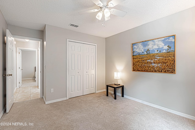 unfurnished bedroom featuring a closet, a textured ceiling, light colored carpet, and ceiling fan