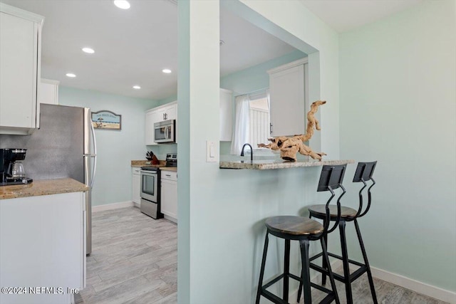 kitchen with light stone countertops, light wood-type flooring, a kitchen bar, stainless steel appliances, and white cabinets