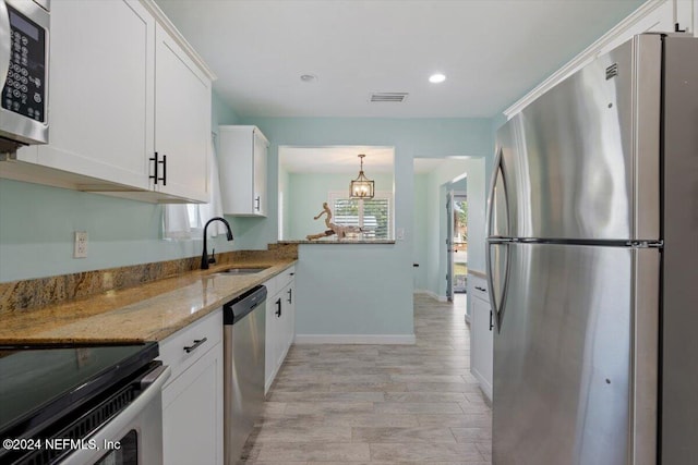 kitchen with appliances with stainless steel finishes, white cabinets, light stone counters, and light hardwood / wood-style floors