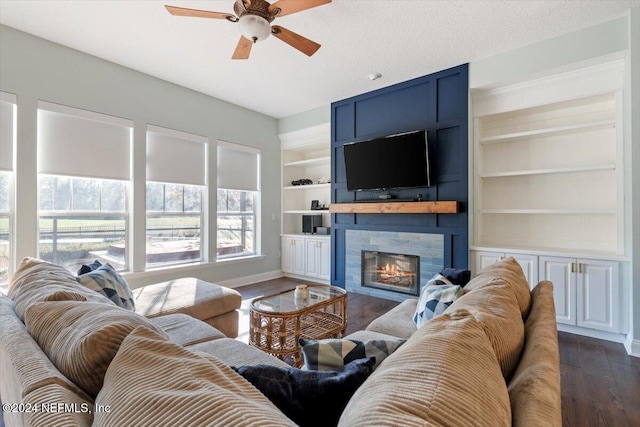 living room featuring dark wood-type flooring, ceiling fan, a fireplace, and built in shelves