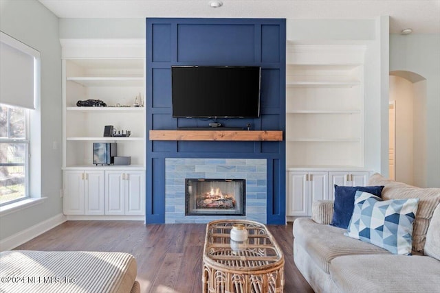 living room with dark wood-type flooring, built in shelves, and a large fireplace