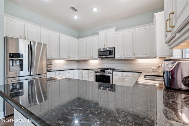 kitchen featuring decorative backsplash, kitchen peninsula, dark stone countertops, white cabinetry, and appliances with stainless steel finishes