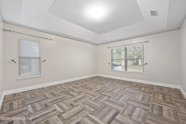 spare room with a textured ceiling, light parquet floors, and a tray ceiling