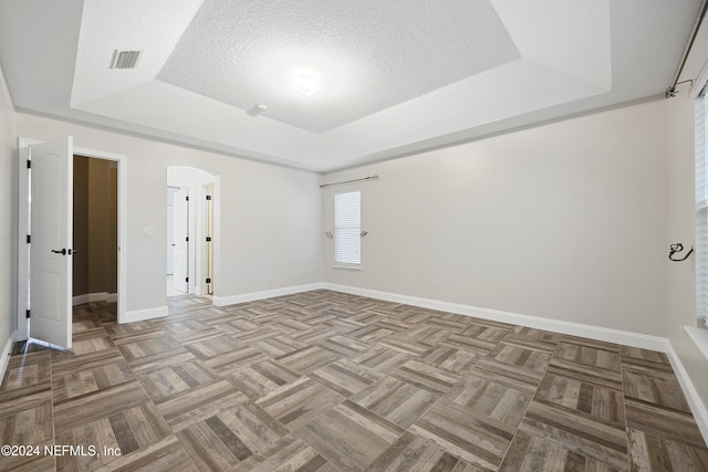 unfurnished room with a textured ceiling, a raised ceiling, and light parquet floors