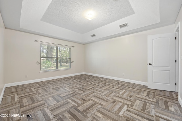 spare room with light parquet floors, a tray ceiling, and a textured ceiling