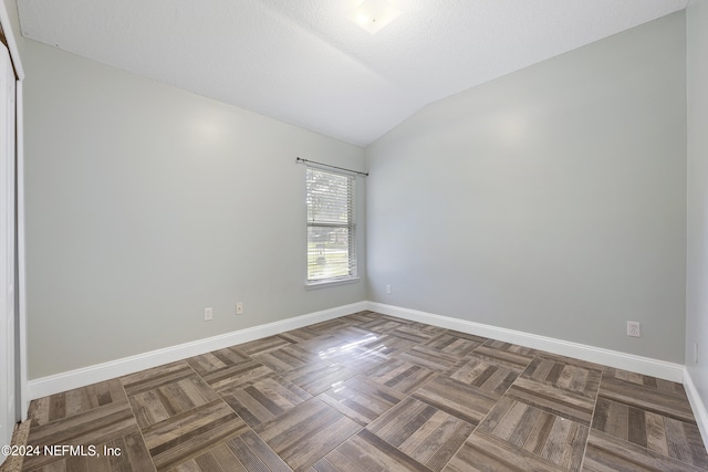 spare room with dark parquet floors, a textured ceiling, and lofted ceiling