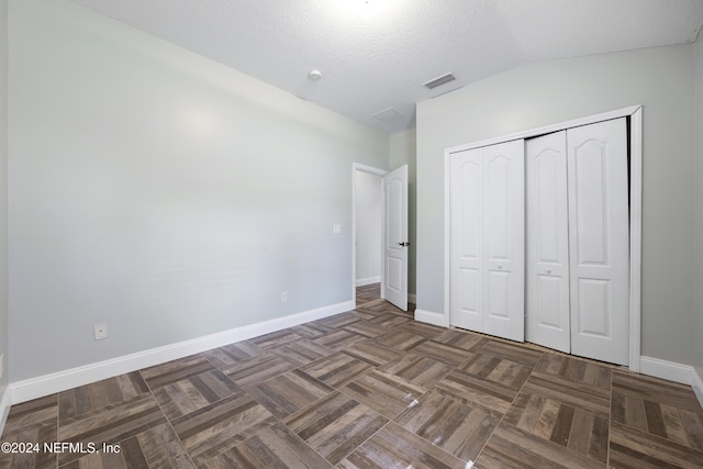 unfurnished bedroom featuring a closet, lofted ceiling, a textured ceiling, and dark parquet flooring