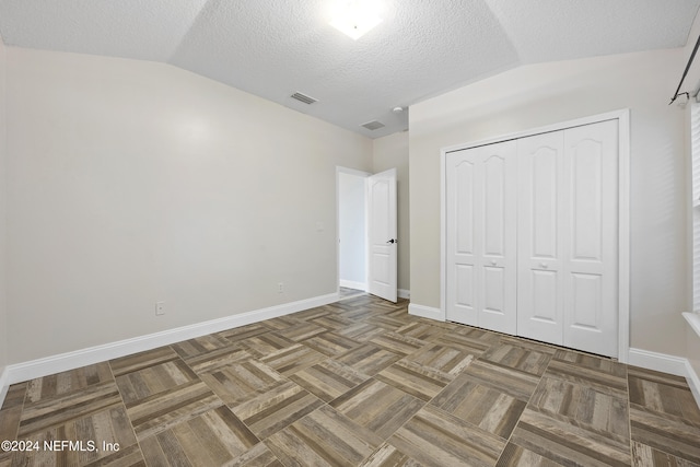 unfurnished bedroom featuring a closet, lofted ceiling, a textured ceiling, and dark parquet flooring