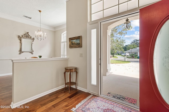 foyer with dark wood-type flooring, a textured ceiling, crown molding, and an inviting chandelier