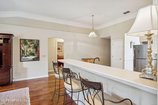 kitchen with stainless steel fridge, a breakfast bar area, dark hardwood / wood-style floors, pendant lighting, and crown molding