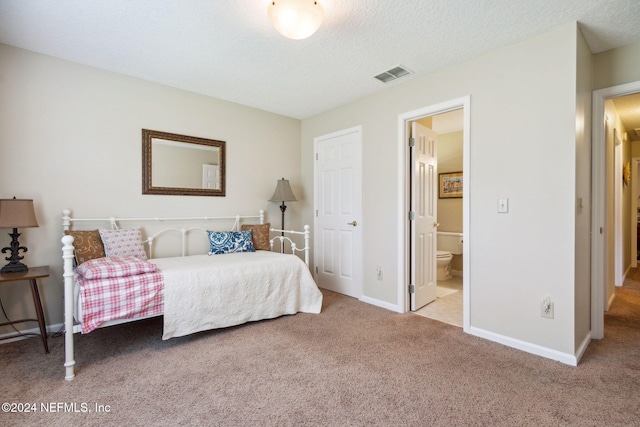 bedroom featuring ensuite bathroom, a textured ceiling, and light colored carpet