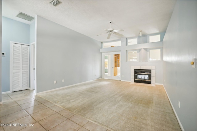 unfurnished living room featuring a tile fireplace, light colored carpet, a textured ceiling, a towering ceiling, and ceiling fan