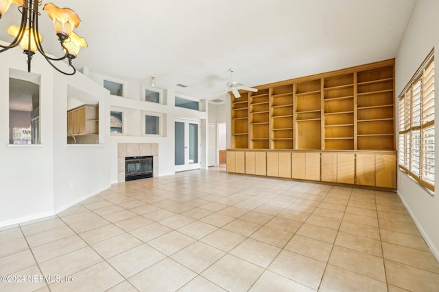 unfurnished living room with built in features, ceiling fan with notable chandelier, a tile fireplace, and light tile patterned floors