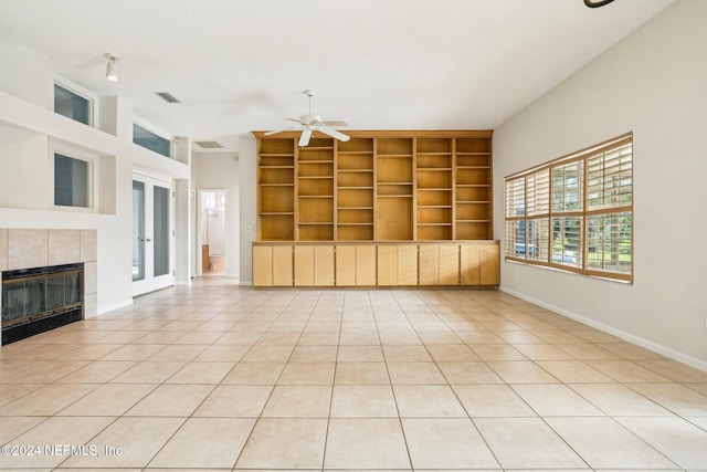 unfurnished living room featuring a tiled fireplace, light tile patterned floors, built in shelves, and ceiling fan