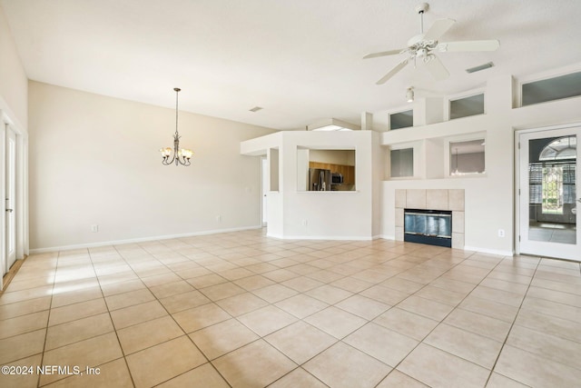 unfurnished living room featuring a towering ceiling, light tile patterned flooring, a tile fireplace, and ceiling fan with notable chandelier