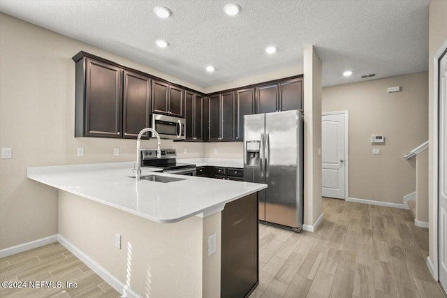 kitchen with kitchen peninsula, a textured ceiling, light wood-type flooring, sink, and stainless steel appliances