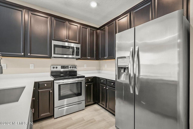 kitchen featuring sink, dark brown cabinets, a textured ceiling, stainless steel appliances, and light hardwood / wood-style flooring