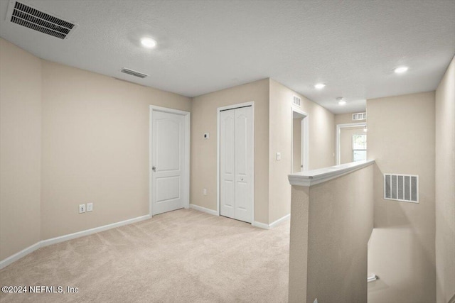 hall featuring light carpet and a textured ceiling