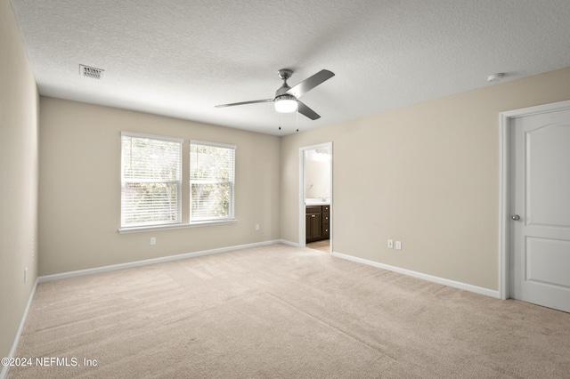 unfurnished bedroom with connected bathroom, ceiling fan, a textured ceiling, and light colored carpet