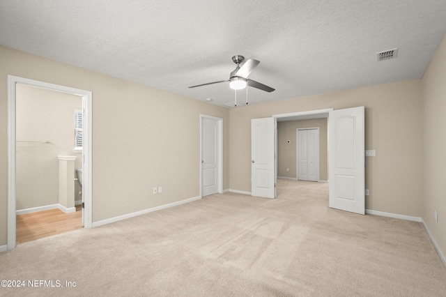 unfurnished bedroom with connected bathroom, a textured ceiling, light colored carpet, and ceiling fan