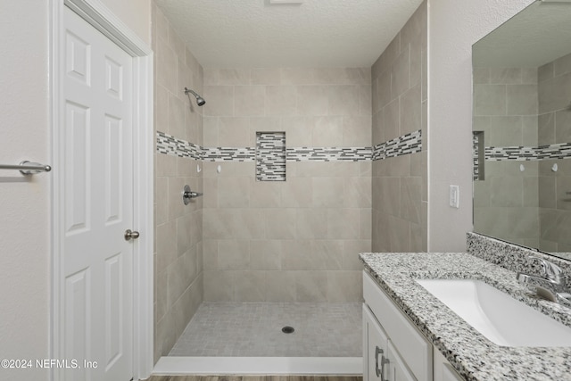 bathroom with vanity, a tile shower, and a textured ceiling