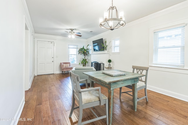 dining area with ornamental molding, ceiling fan with notable chandelier, hardwood / wood-style floors, and a brick fireplace