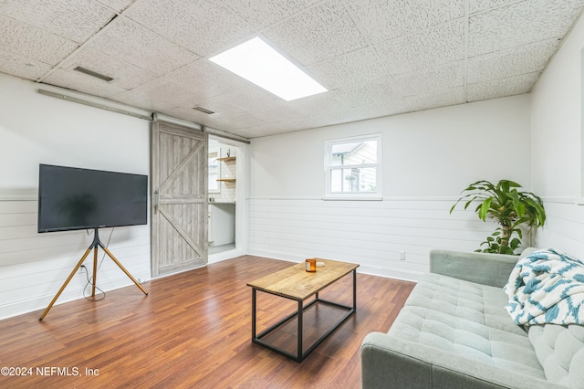 living room with a barn door, hardwood / wood-style floors, and a paneled ceiling