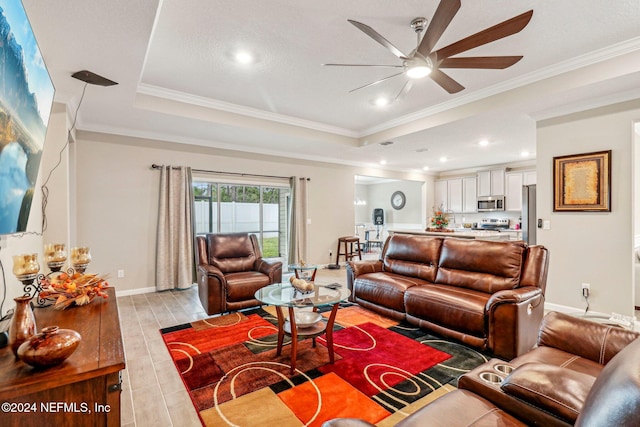 living room with light hardwood / wood-style floors, a raised ceiling, ornamental molding, and ceiling fan