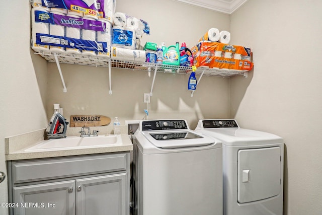 clothes washing area with ornamental molding, sink, washing machine and clothes dryer, and cabinets