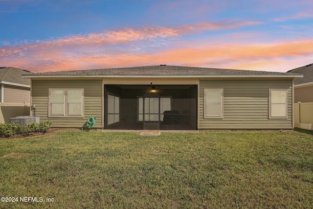 back house at dusk with a yard and central AC unit