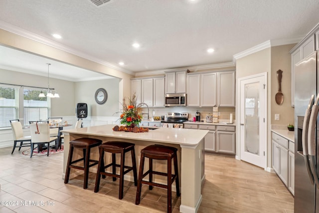 kitchen featuring stainless steel appliances, decorative light fixtures, ornamental molding, a breakfast bar, and a center island with sink