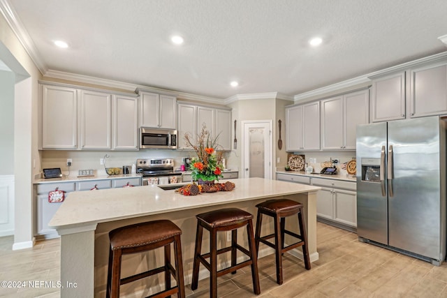 kitchen featuring an island with sink, stainless steel appliances, a breakfast bar, light wood-type flooring, and gray cabinets