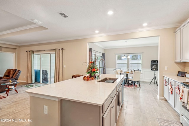 kitchen featuring sink, light hardwood / wood-style floors, light stone counters, ornamental molding, and a center island with sink