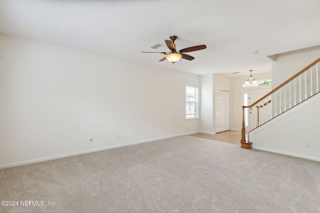 unfurnished living room featuring ceiling fan with notable chandelier, a textured ceiling, and light colored carpet