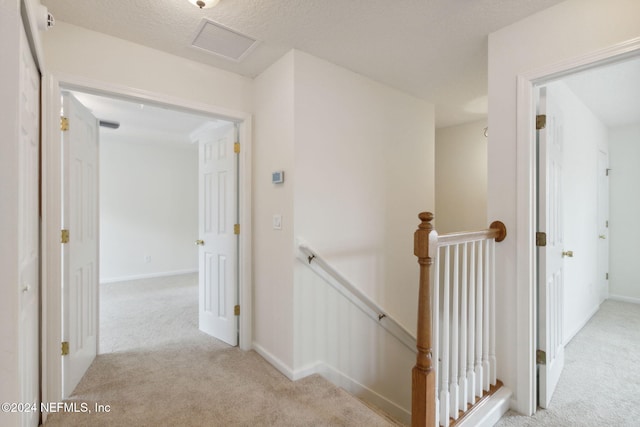 hall featuring a textured ceiling and light colored carpet