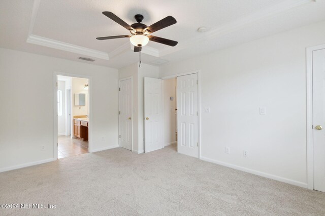 unfurnished bedroom featuring light carpet, ensuite bathroom, a raised ceiling, and ceiling fan