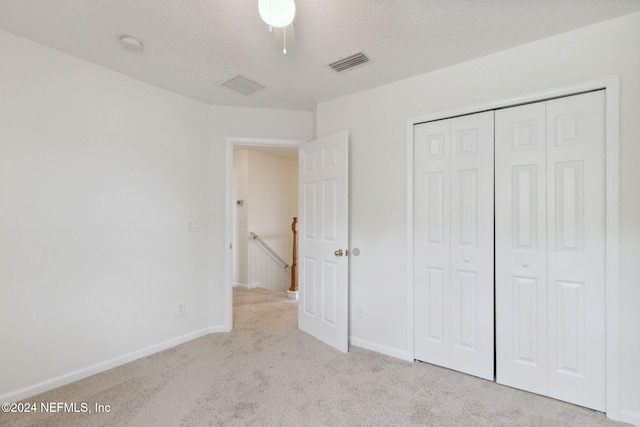 unfurnished bedroom featuring light carpet, a closet, and a textured ceiling