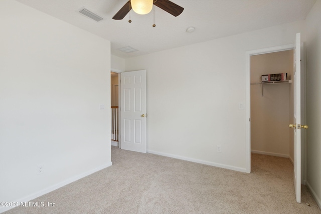 unfurnished bedroom featuring light carpet, a closet, a spacious closet, and ceiling fan