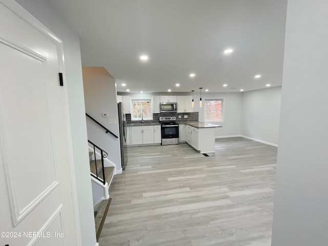 kitchen featuring white cabinets, hanging light fixtures, sink, light wood-type flooring, and appliances with stainless steel finishes