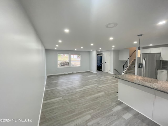 kitchen featuring dark stone counters, stainless steel refrigerator with ice dispenser, hanging light fixtures, light hardwood / wood-style flooring, and white cabinets