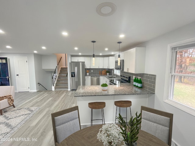 kitchen with backsplash, appliances with stainless steel finishes, pendant lighting, white cabinets, and kitchen peninsula