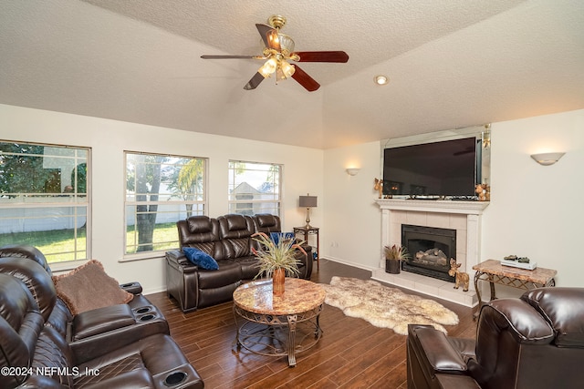 living room featuring lofted ceiling, a tiled fireplace, ceiling fan, a textured ceiling, and dark hardwood / wood-style floors