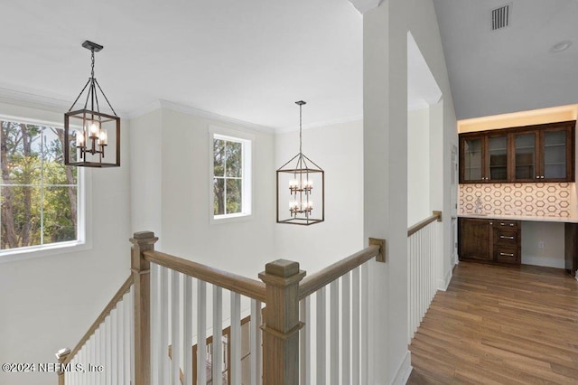 corridor with dark hardwood / wood-style flooring, crown molding, a notable chandelier, and plenty of natural light