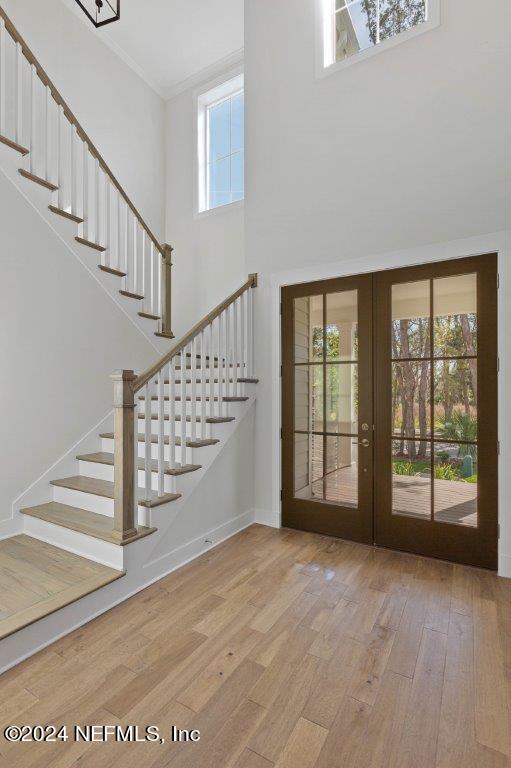 foyer with french doors, crown molding, hardwood / wood-style flooring, and a towering ceiling