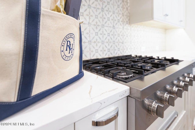 details with white cabinetry, tasteful backsplash, high end range, and light stone counters