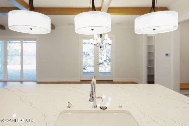 kitchen with beam ceiling, light stone countertops, sink, french doors, and decorative light fixtures