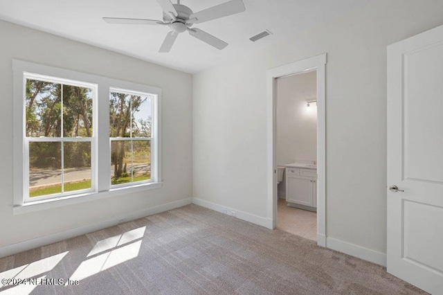 unfurnished bedroom with light carpet, ceiling fan, multiple windows, and ensuite bath