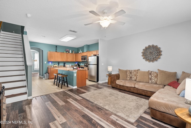 living room featuring a textured ceiling, light wood-type flooring, and ceiling fan